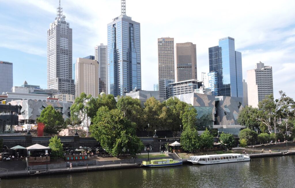 Vibrant view of Melbourne's skyline along the Yarra River featuring iconic skyscrapers and lush greenery.