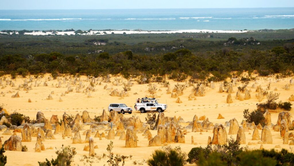 Scenic view of vehicles in the Pinnacles Desert, Western Australia, with ocean in the background.