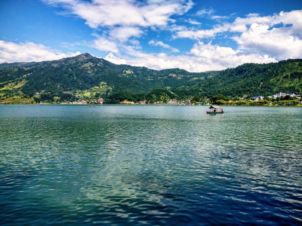 Serene Phewa Lake with lush mountains and clear skies in Pokhara, Nepal.