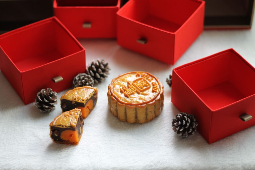 A beautifully arranged display of a mooncake with pine cones and red gift boxes, perfect for the Mid-Autumn Festival.